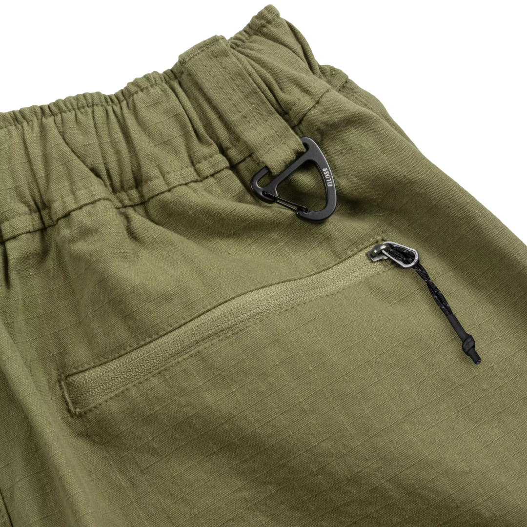 Close-up of olive green outdoor pants showing an elastic waistband, a side zip pocket, and black carabiner-style hardware on a white background.