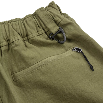 Close-up of olive green outdoor pants showing an elastic waistband, a side zip pocket, and black carabiner-style hardware on a white background.