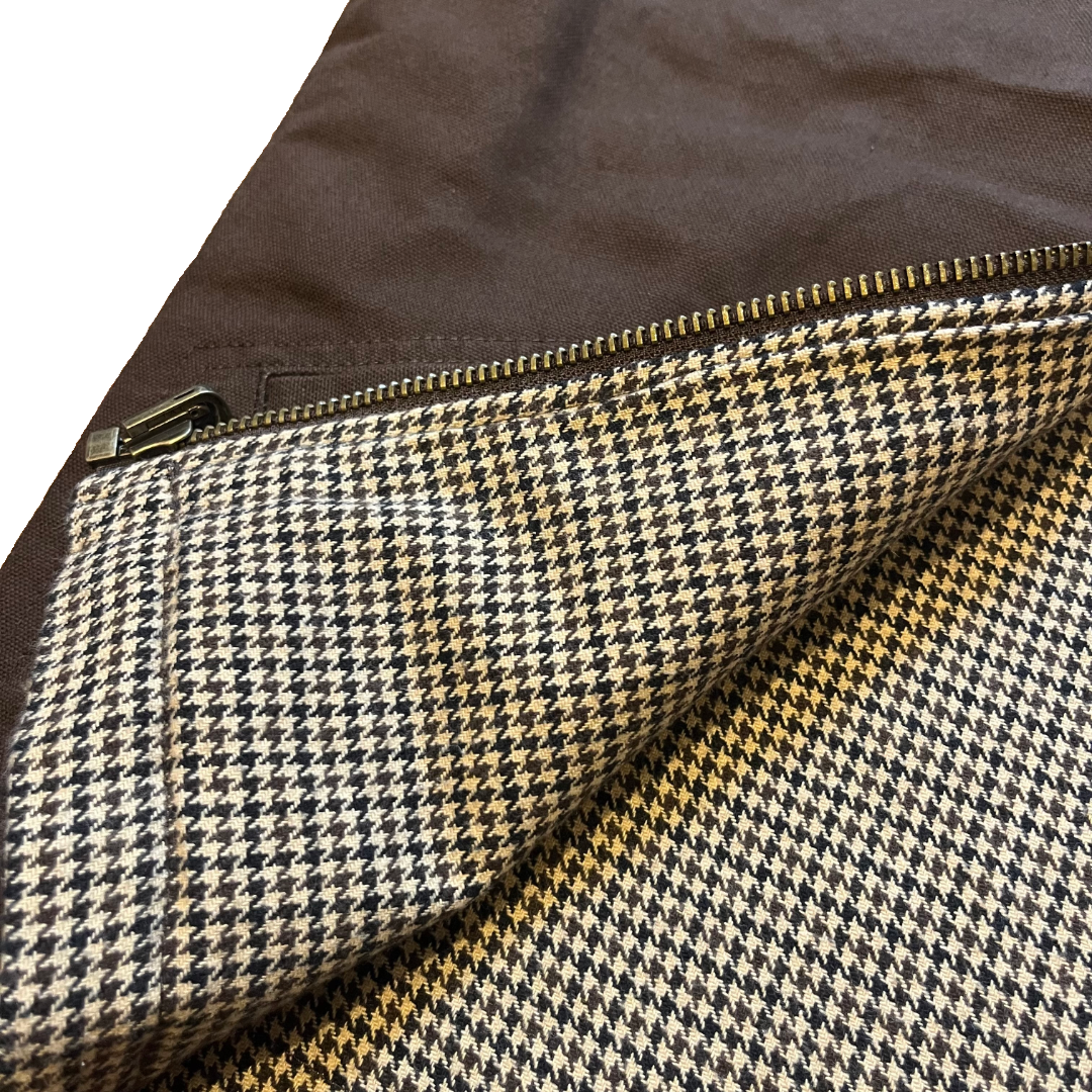 Close-up of a houndstooth fabric with a brown zipper, showing a pattern of black, beige, and white, with a solid brown background.