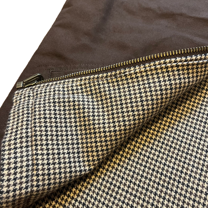 Close-up of a houndstooth fabric with a brown zipper, showing a pattern of black, beige, and white, with a solid brown background.