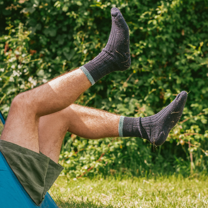 A person reclining outdoors in a blue hammock, wearing dark charcoal gray ribbed crew socks with light gray elastic cuffs, set against a background of green grass and foliage.