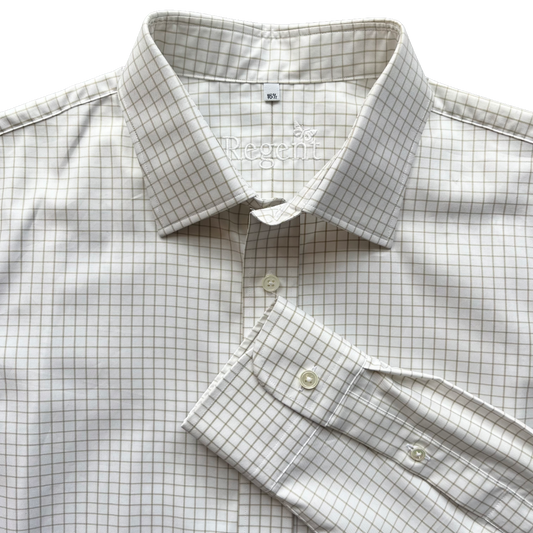 A close-up of a long-sleeve dress shirt with a fine brown grid pattern on a white base, featuring a pointed collar, button-down front, and a folded cuff.