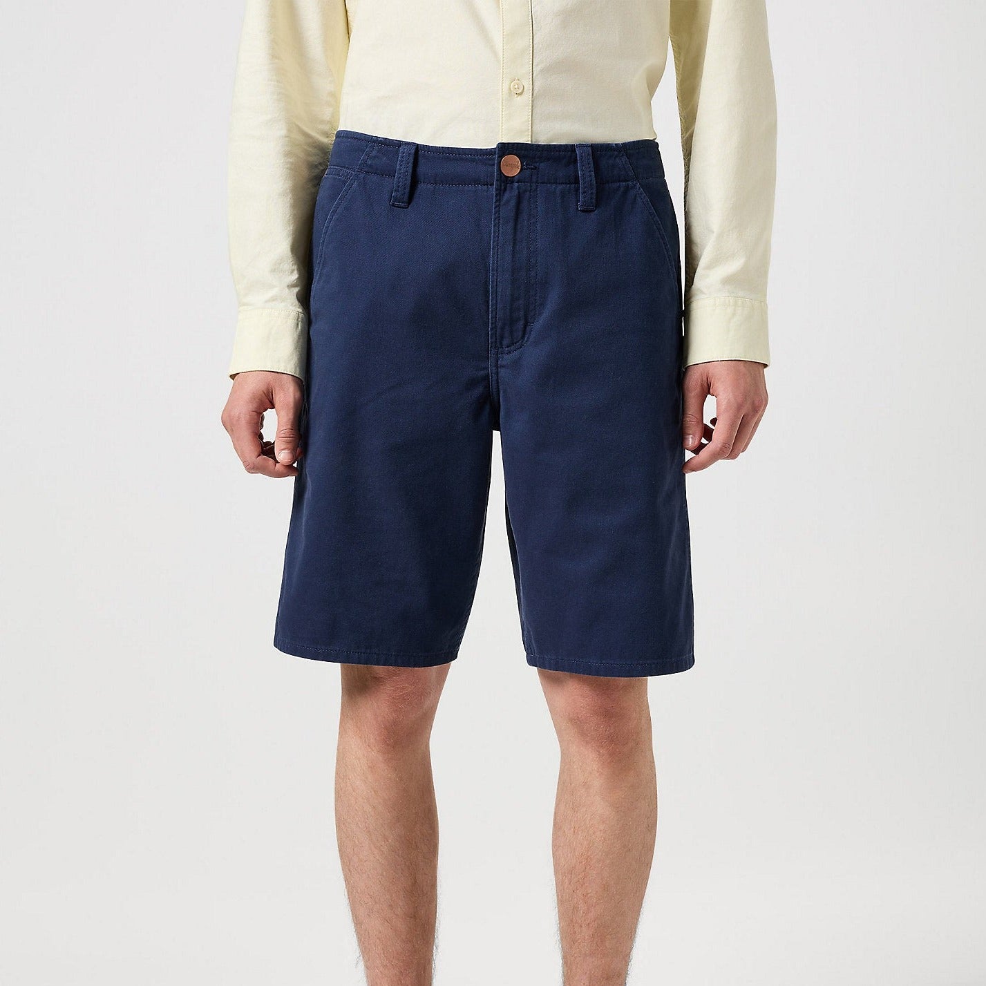 Blue Wrangler Casey Jones Chino Shorts shown on the torso of a man - worn with a cream coloured shirt and stood against a plain background