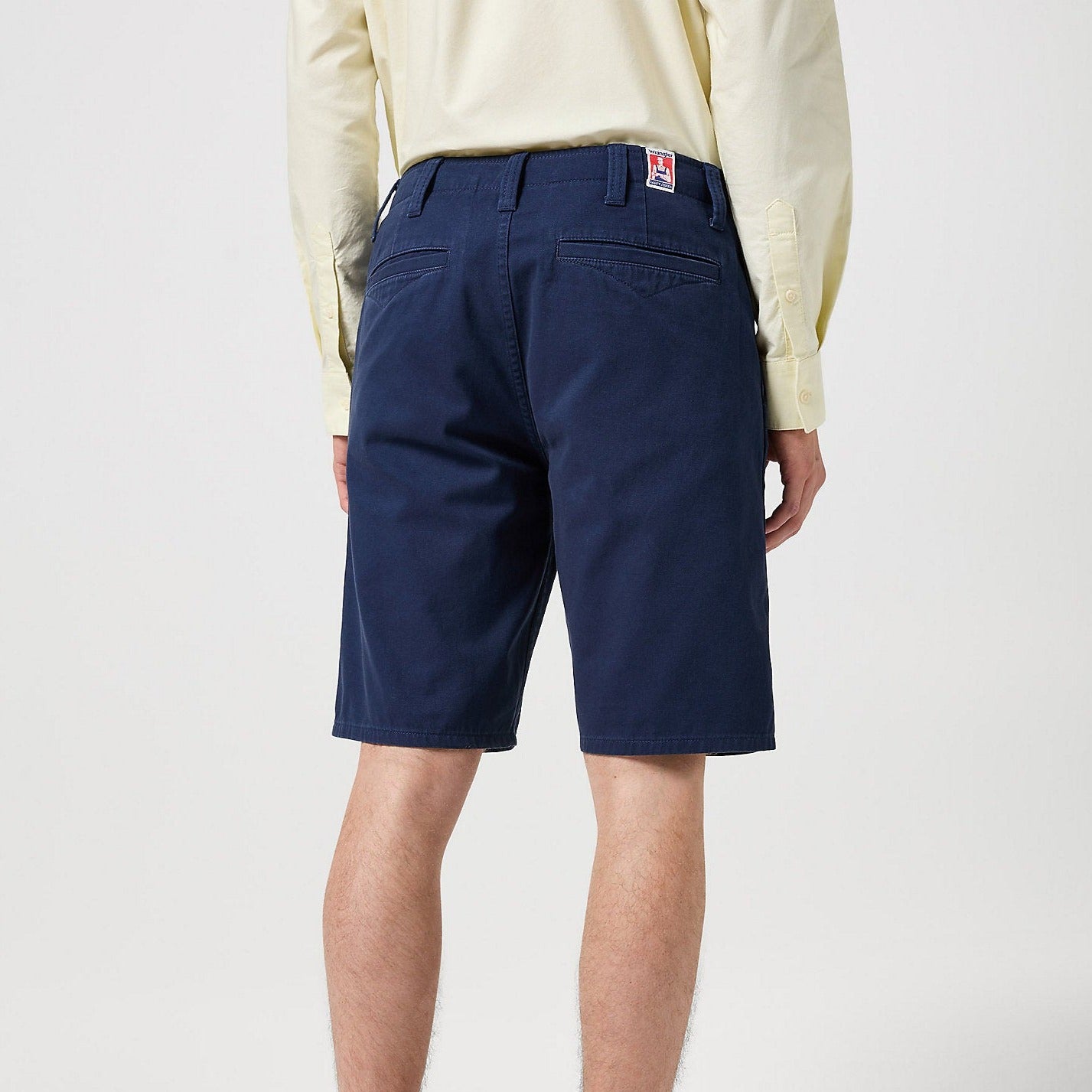 Rear of blue Wrangler Casey Jones Chino Shorts shown on the torso of a man - worn with a cream coloured shirt and stood against a plain background