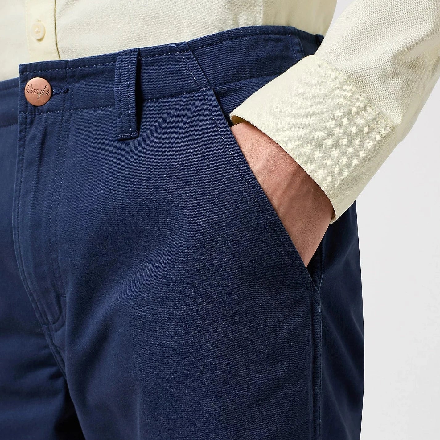 Close up of the pocket of Blue Wrangler Casey Jones Chino Shorts shown on the torso of a man - worn with a cream coloured shirt and stood against a plain background