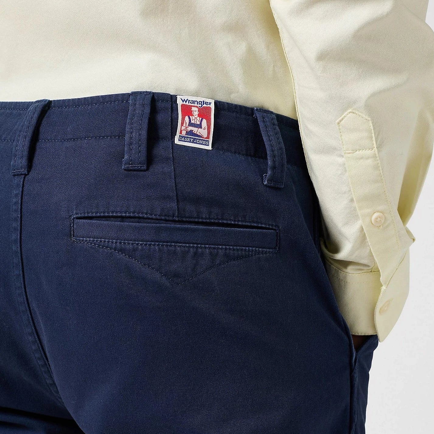 Blue Wrangler Casey Jones Chino Shorts shown on the torso of a man - worn with a cream coloured shirt and stood against a plain background