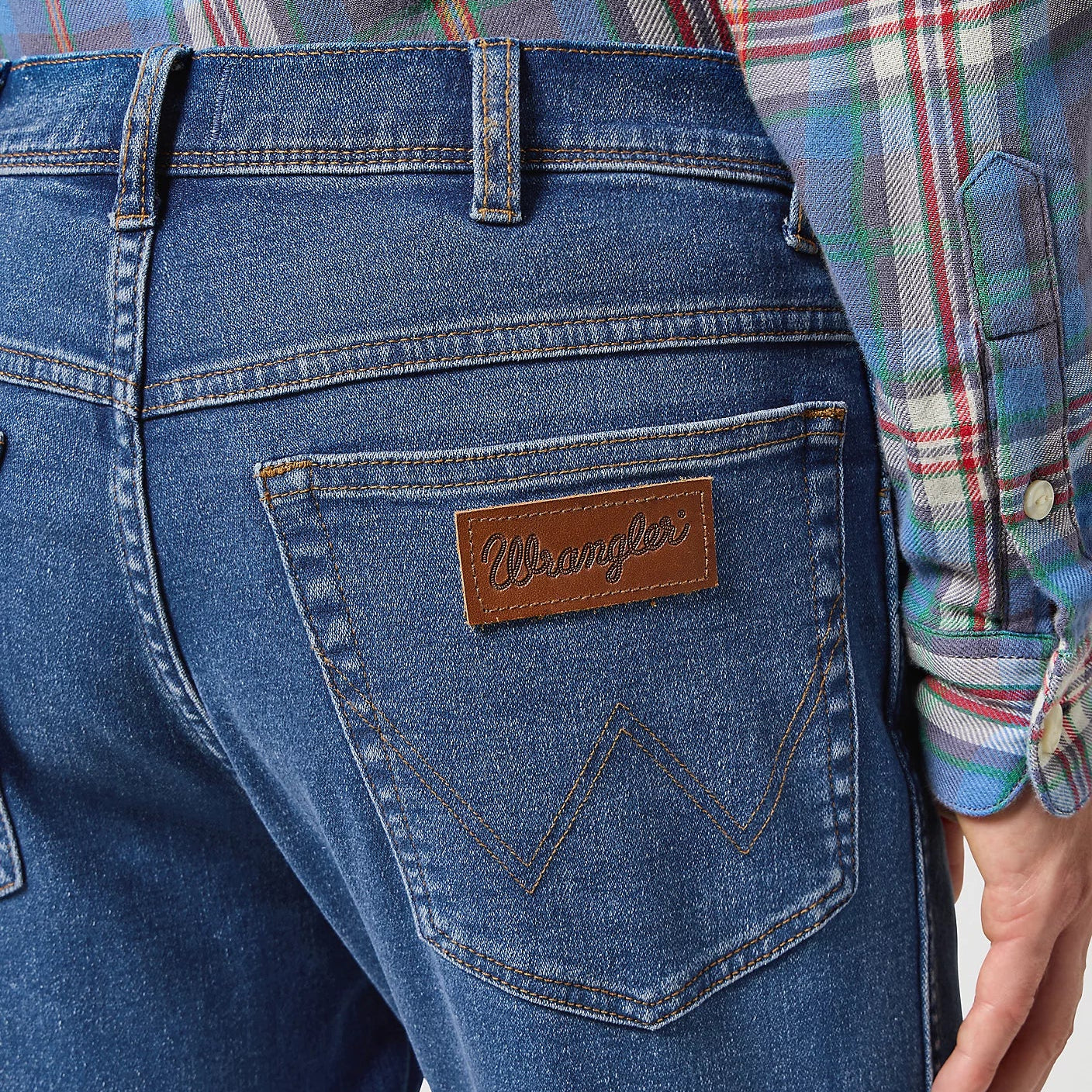 Close-up of blue jeans with a brand logo, worn by a person in a plaid shirt.