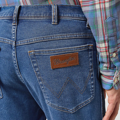 Close-up of blue jeans with a brand logo, worn by a person in a plaid shirt.