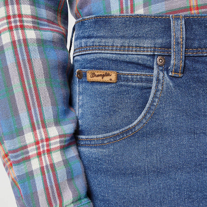 Close-up of blue jeans with a brand logo and a plaid shirt sleeve.