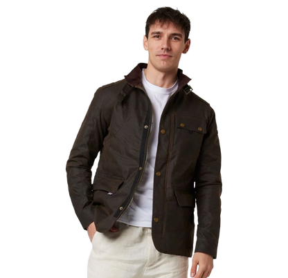 A man wearing a dark brown waxed cotton utility jacket with a white t-shirt and off-white trousers, standing against a solid white background.
