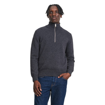 A man wearing a dark gray quarter-zip knit sweater and blue jeans, standing against a plain white background.