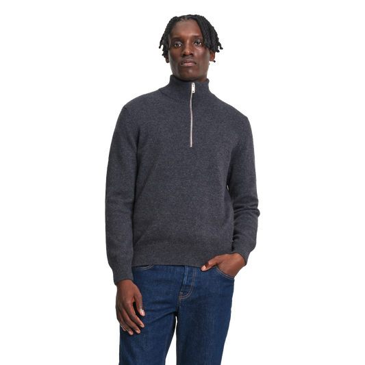 A man wearing a dark gray quarter-zip knit sweater and blue jeans, standing against a plain white background.