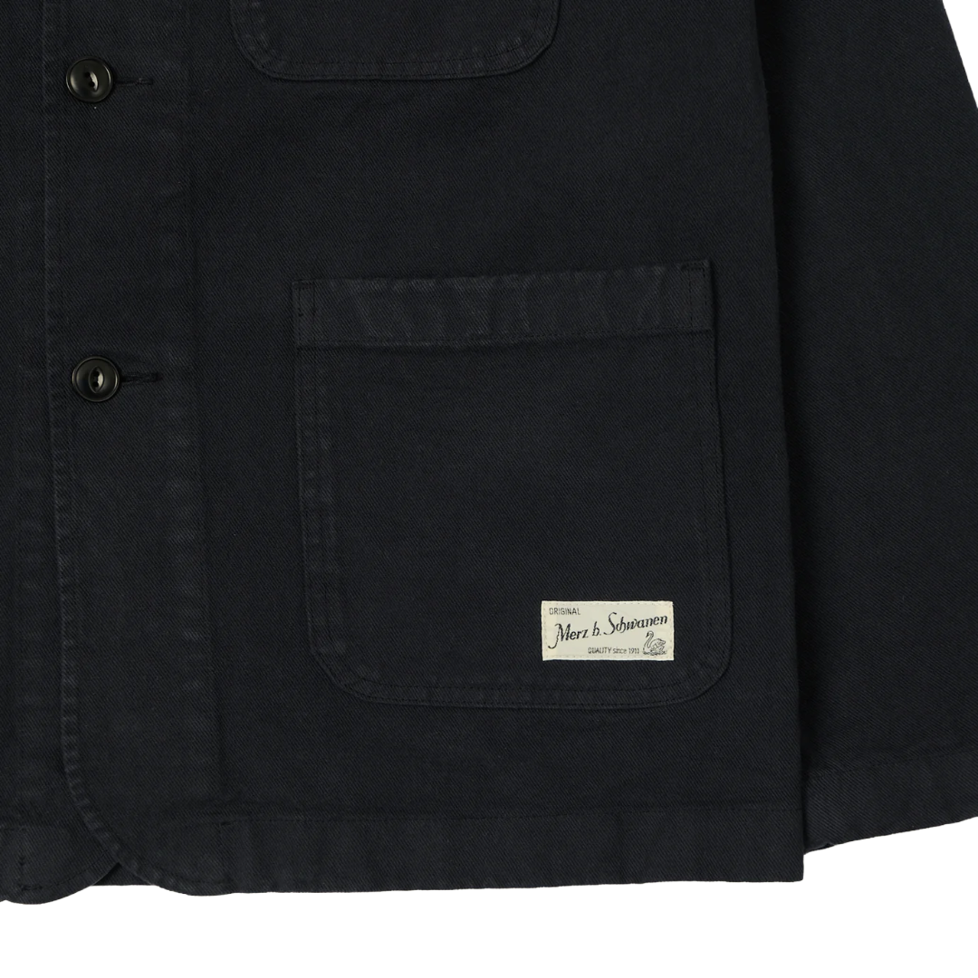 Close-up of a charcoal canvas utility jacket showing a front button closure, a large chest pocket.
