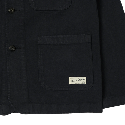 Close-up of a charcoal canvas utility jacket showing a front button closure, a large chest pocket.