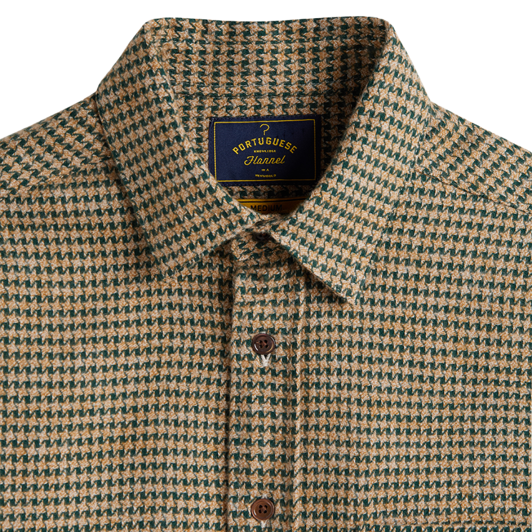 Close-up of a collared button-up shirt with a small-scale houndstooth pattern in beige and dark green. The shirt features a dark blue neck label with gold lettering that reads 'PORTUGUE Houndstooth'.