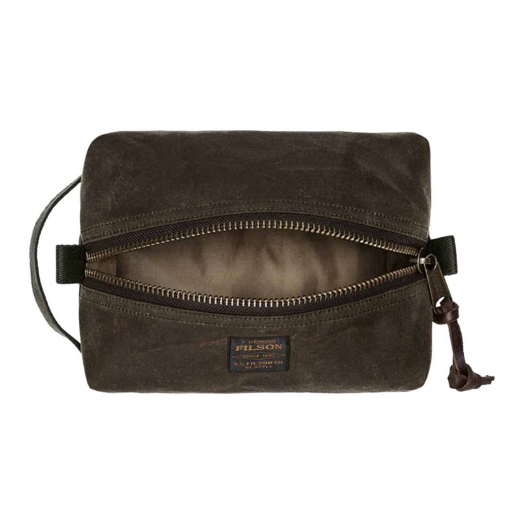 A dark brown Filson waxed canvas pouch with an open top zipper, showing a beige interior lining. The Filson brand label is visible on the front, and a leather zipper pull hangs on the right side against a plain white background.