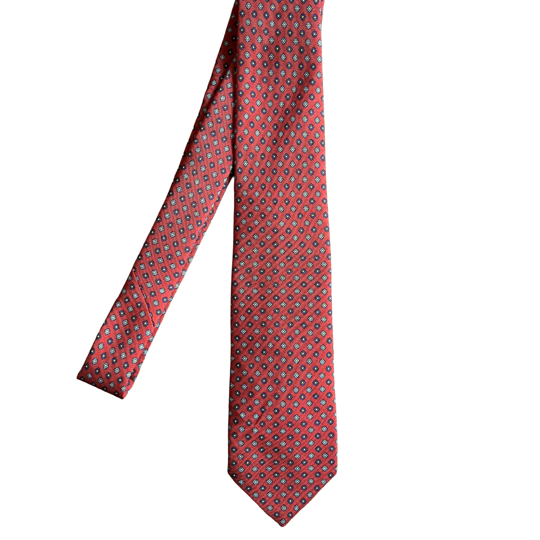 A red necktie with a repeating geometric medallion pattern in black, white, and blue, shown against a plain white background.
