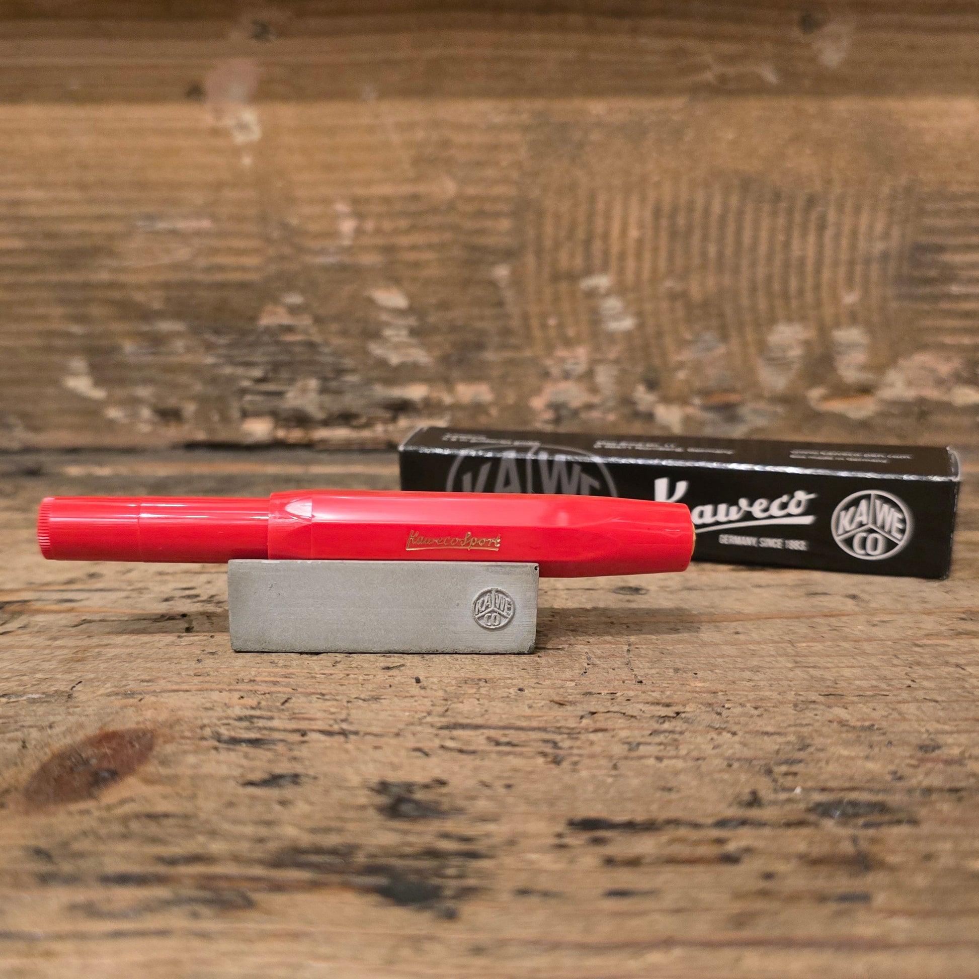 Red Kaweco Pen on Wooden block with its box behind it on a wooden background