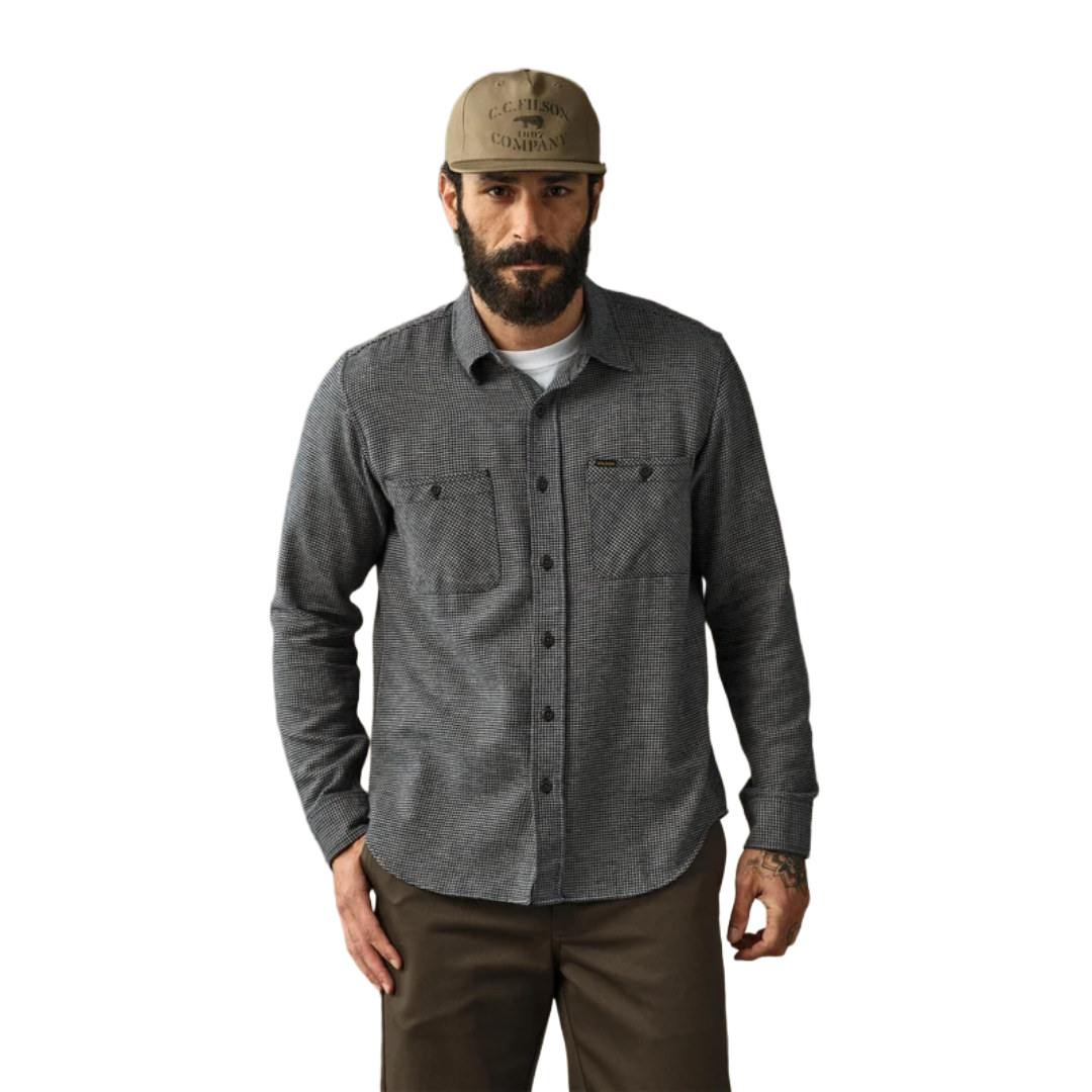 A man wearing a dark gray long-sleeve button-up shirt with two chest pockets, a tan baseball cap, and brown pants, standing against a plain white background.