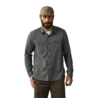 A man wearing a dark gray long-sleeve button-up shirt with two chest pockets, a tan baseball cap, and brown pants, standing against a plain white background.