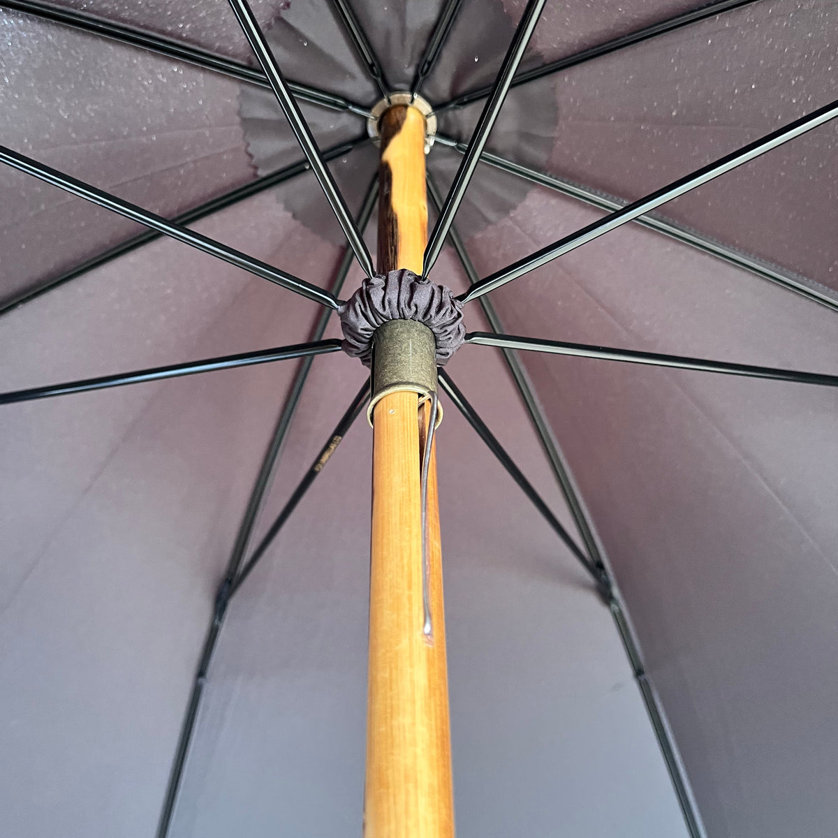 Close-up view from inside a large umbrella showing the wooden handle, black metal ribs, and gray fabric canopy.