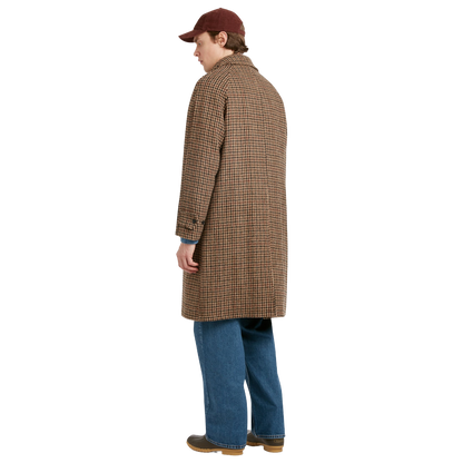 A person shown from the back wearing a brown and tan houndstooth patterned coat, blue jeans, brown shoes, and a dark red baseball cap, against a plain white background.