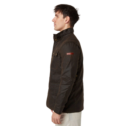 A man shown in profile wearing a dark brown waxed cotton jacket with a small red Barbour logo patch on the upper sleeve, paired with off-white trousers, against a plain white background.