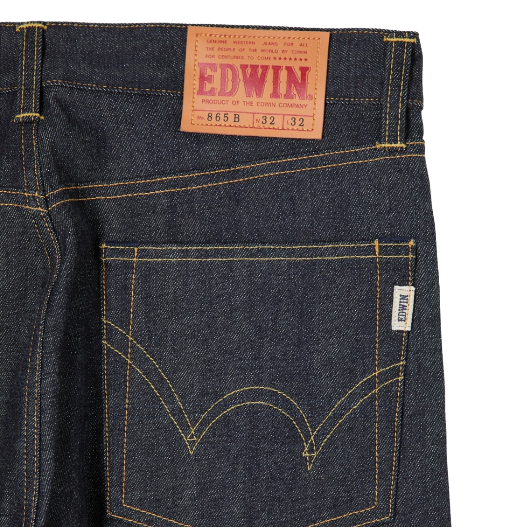 Close-up of the back waistband and rear pocket of dark indigo denim jeans with contrast yellow stitching, a tan leather EDWIN waist patch, and a small white brand tag.