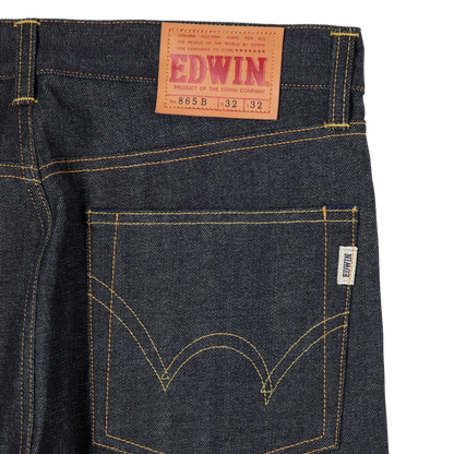 Close-up of the back waistband and rear pocket of dark indigo denim jeans with contrast yellow stitching, a tan leather EDWIN waist patch, and a small white brand tag.