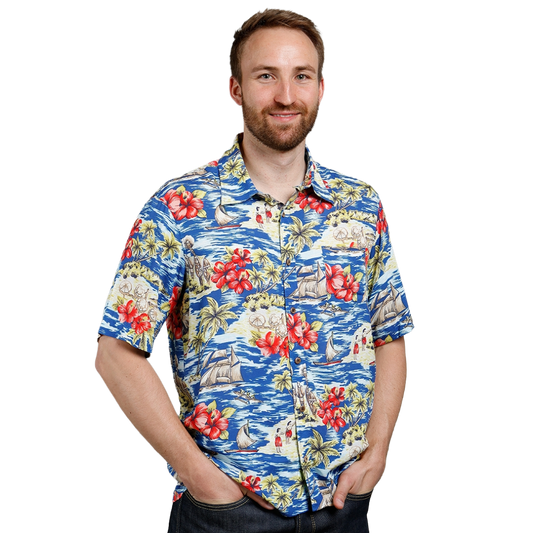 A man wearing a short-sleeve button-up Hawaiian shirt with a vibrant blue ocean, white sailboats, and red hibiscus flowers pattern, photographed against a solid white background.