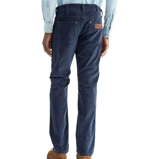 Rear view of a person wearing dark blue corduroy pants with a brown leather patch on the back pocket, paired with a light blue shirt and brown shoes, against a white background.