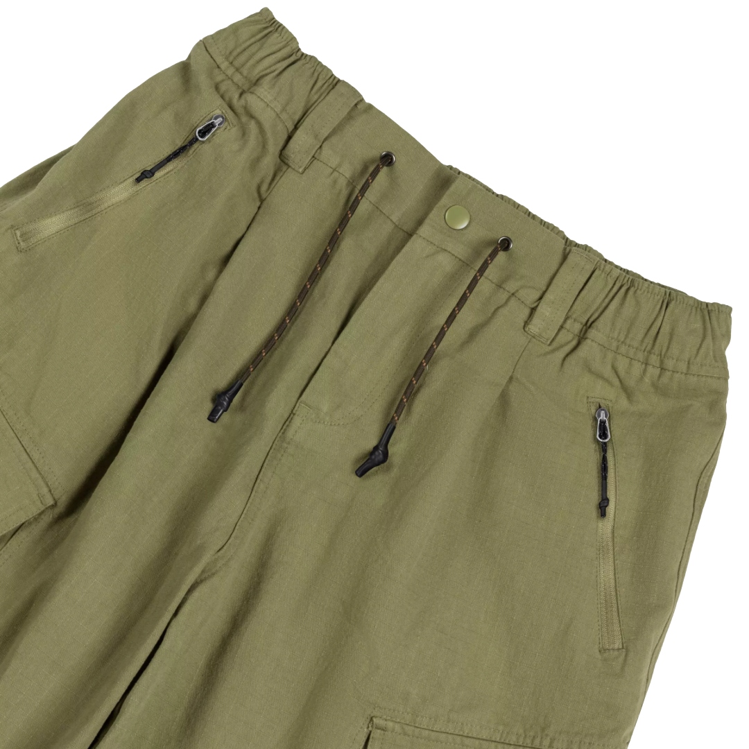 Close-up of olive green drawstring pants showing the elastic waistband, zippered pockets, and dark brown drawstrings against a white background.