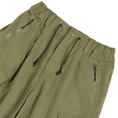 Close-up of olive green drawstring pants showing the elastic waistband, zippered pockets, and dark brown drawstrings against a white background.
