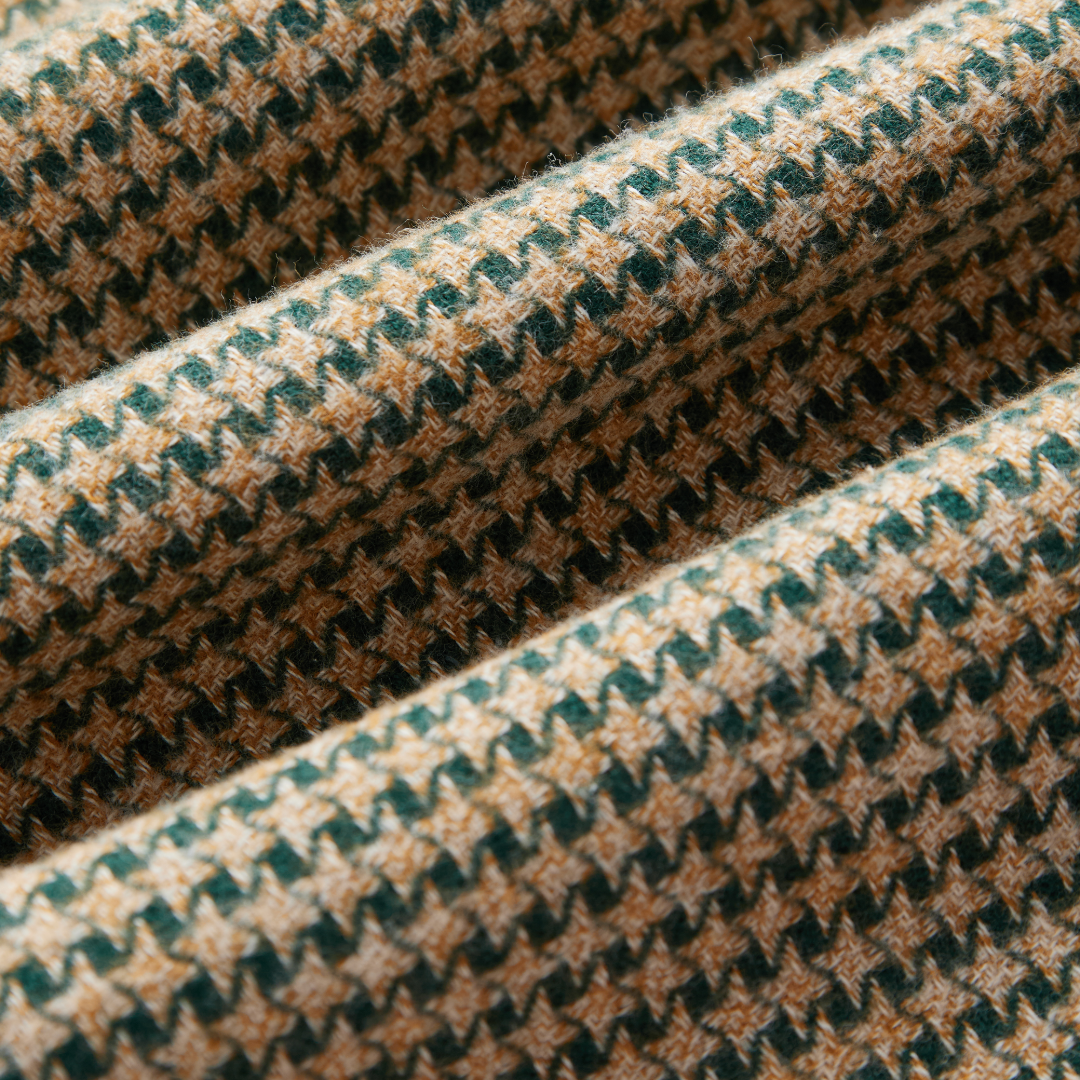 A close-up of a textured fabric with a woven houndstooth pattern in beige, brown, and dark green.