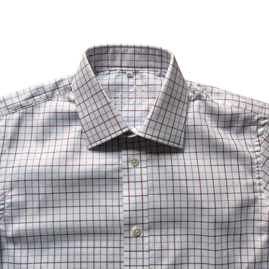 A close-up of a men's dress shirt with a white base, featuring a subtle blue and dark red windowpane check pattern. The shirt is styled with a spread collar and button-down front, with the brand name 'L'ECOMME' visible on the inner neck label.
