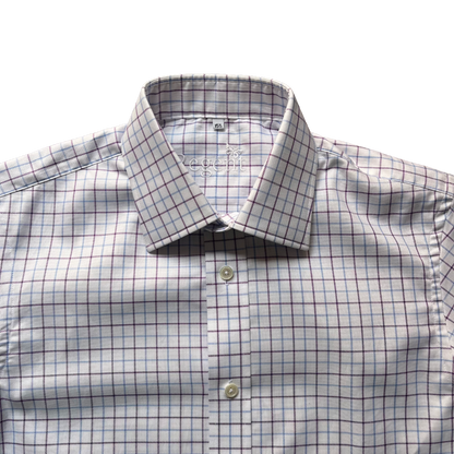 A close-up of a men's dress shirt with a white base, featuring a subtle blue and dark red windowpane check pattern. The shirt is styled with a spread collar and button-down front, with the brand name 'L'ECOMME' visible on the inner neck label.