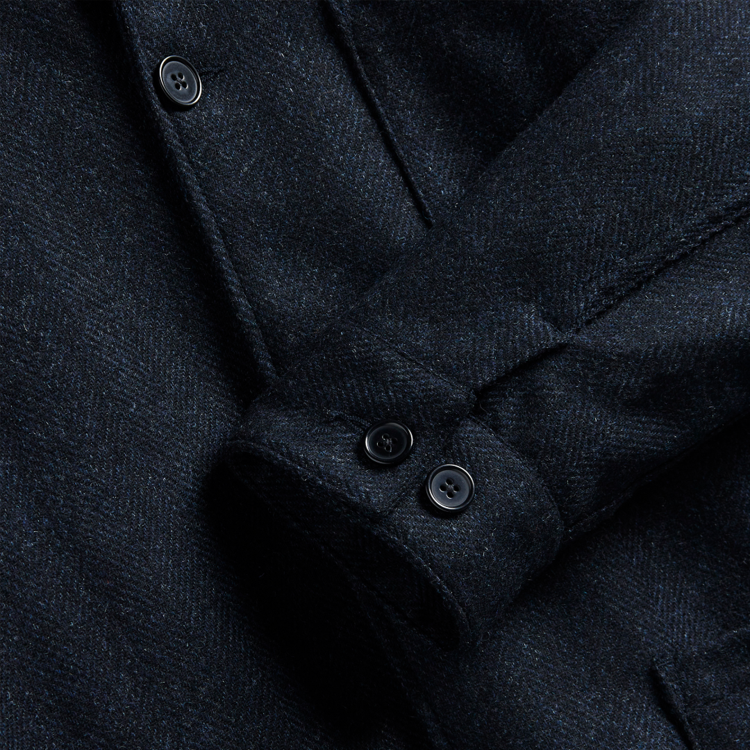 Close-up of a dark navy textured fabric garment, showing the weave detail and buttoned cuff with dark buttons.