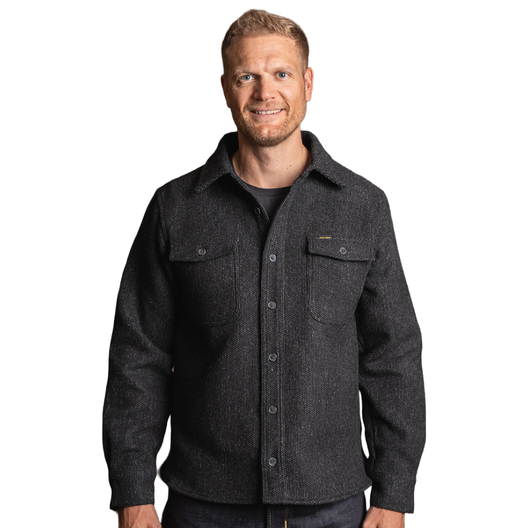 A man wearing a dark charcoal gray textured button-up overshirt with chest pockets, photographed against a solid white background.