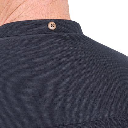 Close-up of the back collar of a dark navy textured shirt, showing a single brown button and the back of a person's neck.