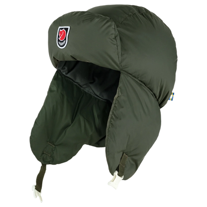 An olive green padded military-style trapper hat with ear flaps and chin straps, featuring a red and black shield logo on the side, shown against a plain white background.
