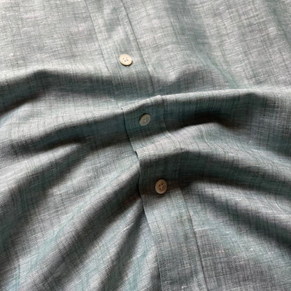 Close-up of a textured linen shirt in a muted sage green color, showing the fabric weave and three buttons.
