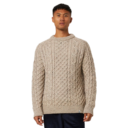 A man wearing a beige cable-knit crewneck sweater, standing against a plain white background.