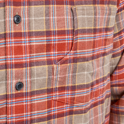 Close-up of a plaid button-up shirt fabric with a chest pocket and dark buttons, showing a pattern of rust red, tan, brown, light blue, and white.