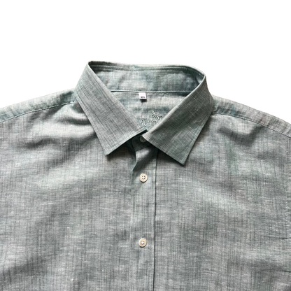 A close-up of a men's long-sleeve button-down shirt in a textured sage green fabric, showing the collar, button placket, and inner neck label.