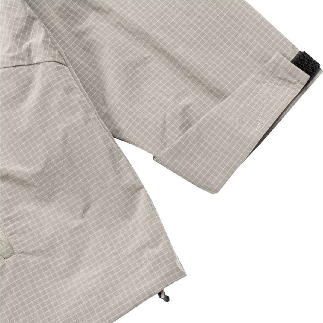 Close-up of a light gray and white grid-patterned garment, showing the fabric texture, a cuff with a black hook-and-loop tab, and a small black adjustment loop near the hem, set against a plain white background.