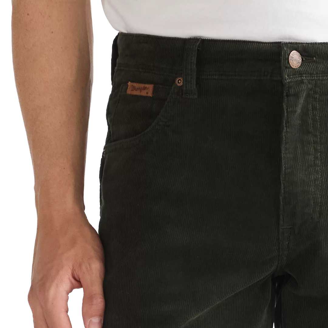 Close-up of a person wearing dark olive corduroy pants, showing the front pocket with a brown leather Levi's brand tab, a white shirt at the waist, and a silver button.