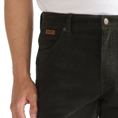 Close-up of a person wearing dark olive corduroy pants, showing the front pocket with a brown leather Levi's brand tab, a white shirt at the waist, and a silver button.