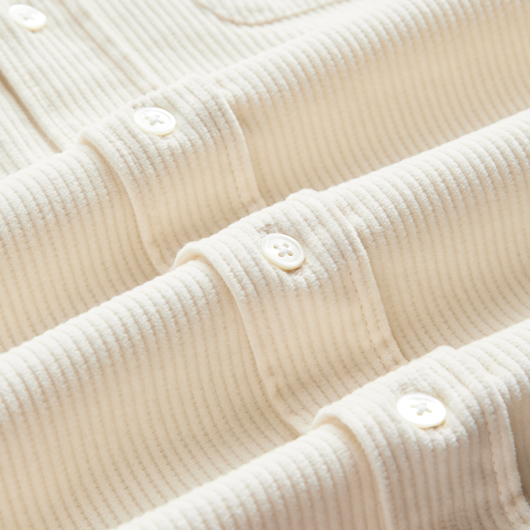 Close-up of a cream-colored ribbed knit top with buttoned collar details and a visible corduroy texture.