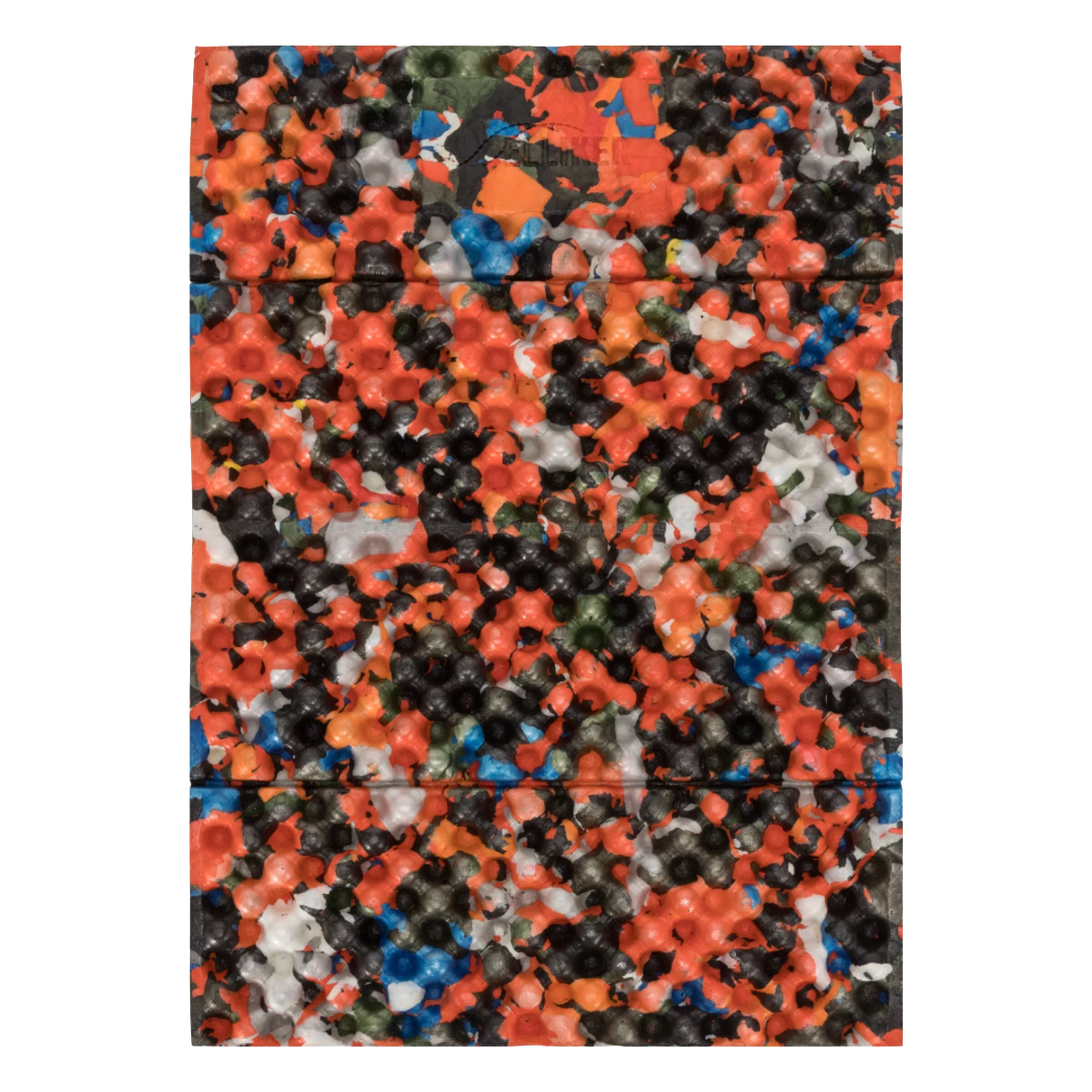 A rectangular product with rounded corners, covered in a dense, multicolored textured pattern of small star- and flower-like shapes. The colors include orange, black, blue, white, and green in roughly equal prominence, creating a highly speckled, multicolor effect.