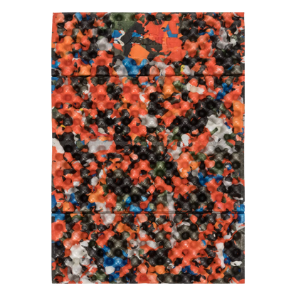 A rectangular product with rounded corners, covered in a dense, multicolored textured pattern of small star- and flower-like shapes. The colors include orange, black, blue, white, and green in roughly equal prominence, creating a highly speckled, multicolor effect.